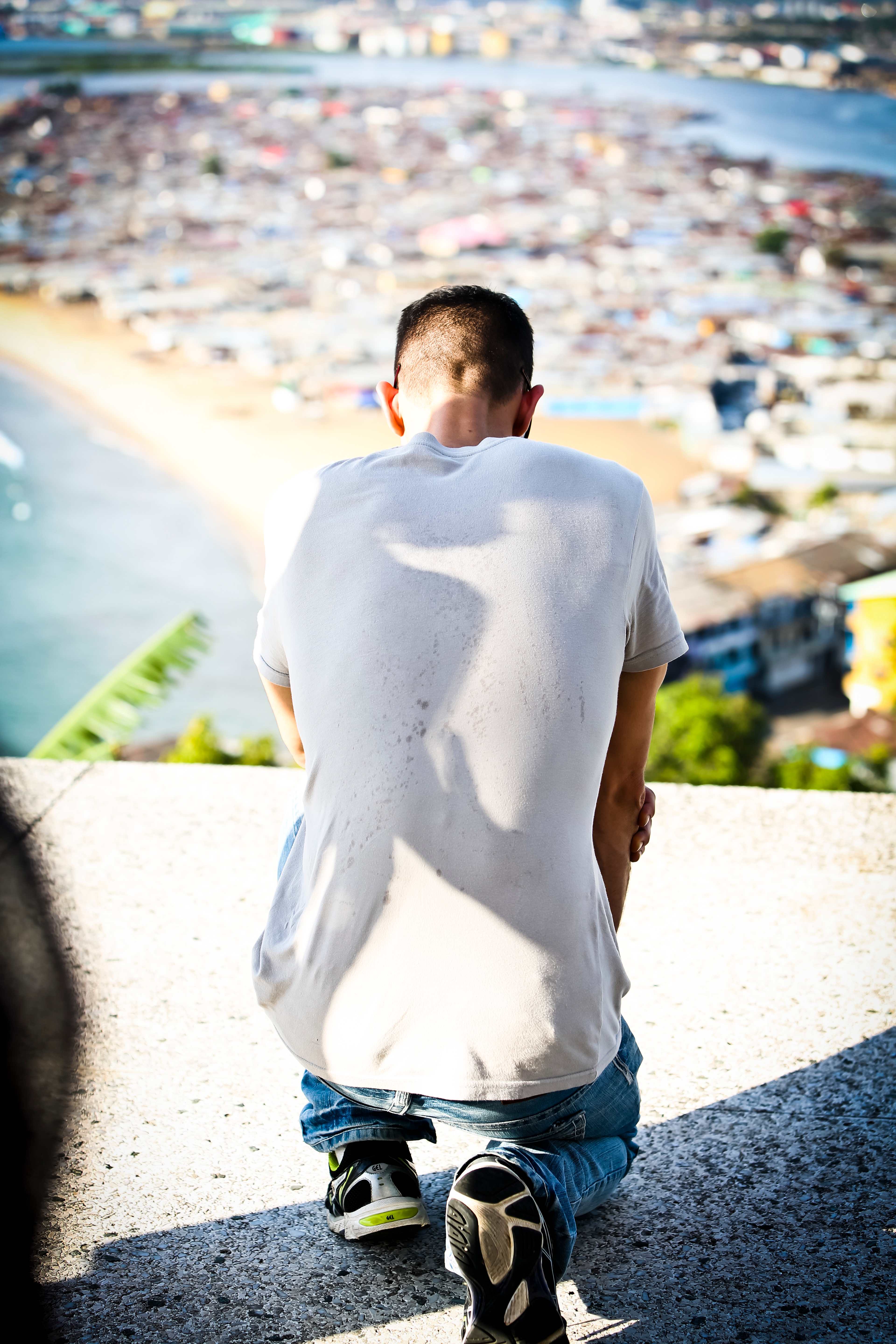 Person in white shirt sitting and looking over coastal city, contemplative view of achievement and vision
