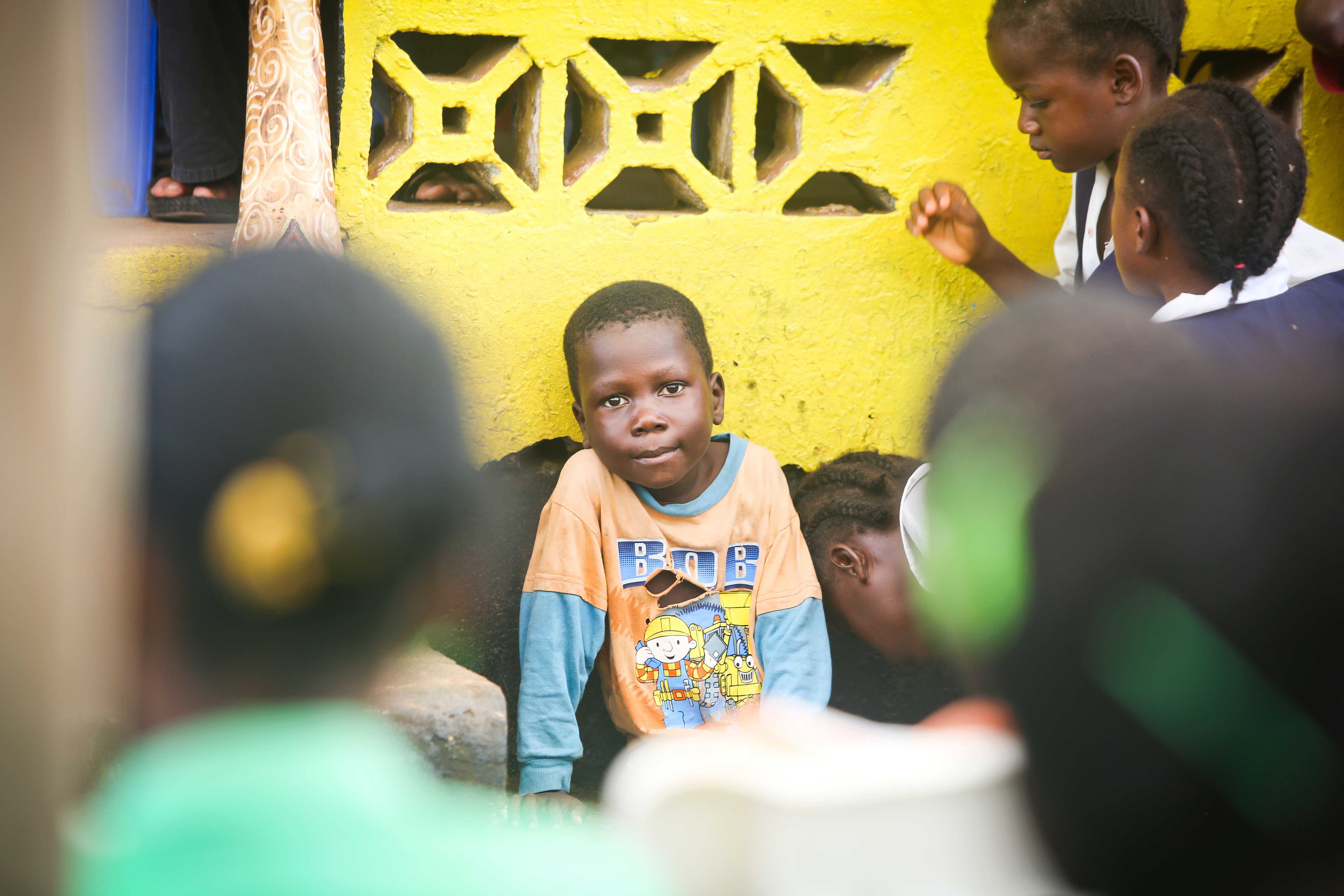 children in African community setting, young boy in orange and blue shirt, community development